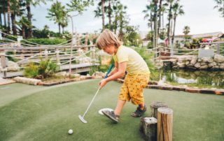 A kid playing mini golf in Naples.